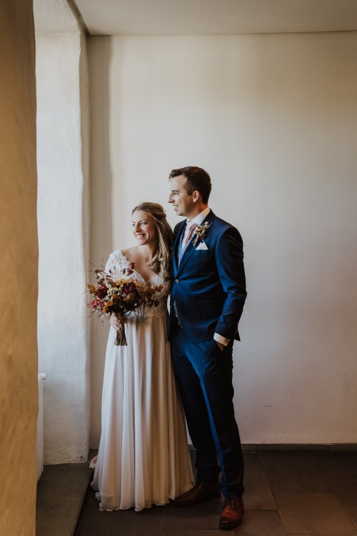 Ein Brautpaar steht vor einem Fenster.