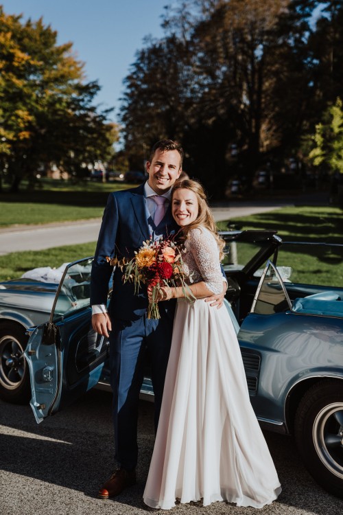Ein Brautpaar posiert für ein Foto vor einem Auto.