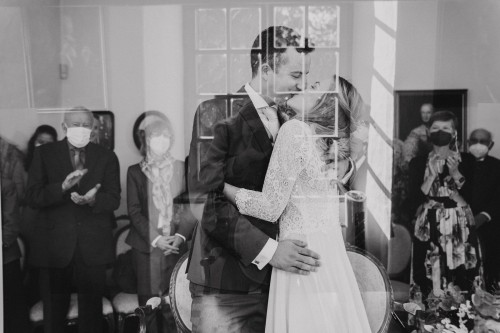 Ein schwarz-weißes Bild von einem küssenden Brautpaar und deren Gästen im Hintergrund.