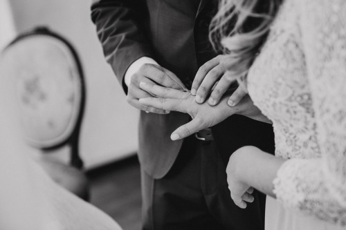 Ein schwarz-weißes Bild von einem Bräutigam der einer Braut einen Ehering ansteckt.