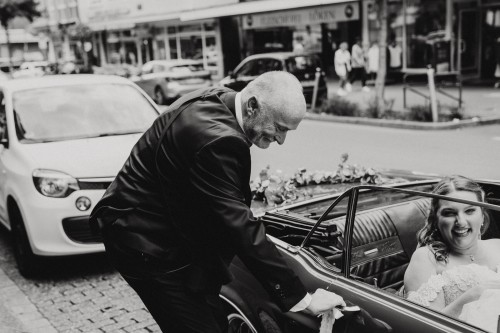 Ein Mann öffnet die Tür am Auto damit die Braut aussteigen kann.