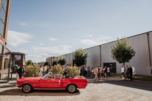 Eine Gruppe von Menschen und ein rotes Auto vor einem Gebäude.