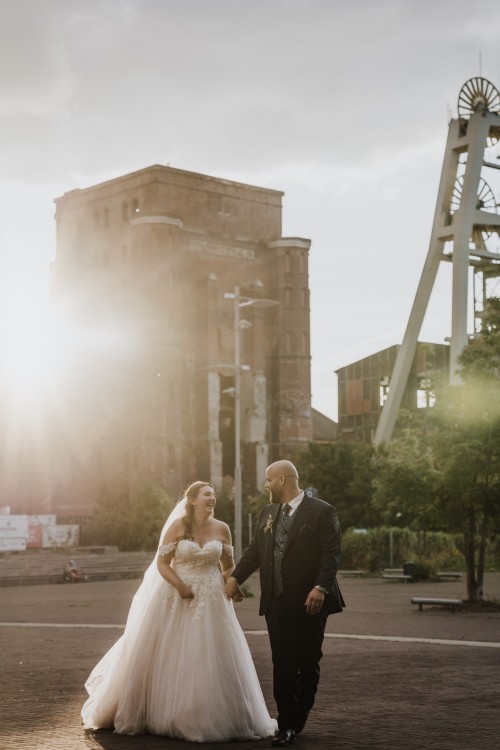 Eine Braut und ein Bräutigam spazieren vor einer Zeche.