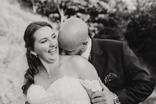 Ein Bräutigam knabbert an dem Hals der Braut.