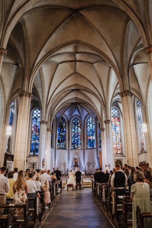Ein Brautpaar und eine Gruppe von Menschen stehen mitten in einer Kirche.