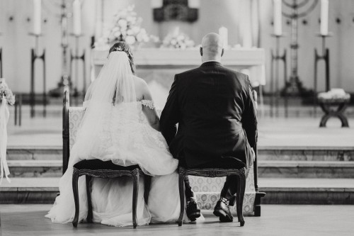 Ein schwarz-weißes Bild von einem Brautpaar das in einer Kirche sitzt.