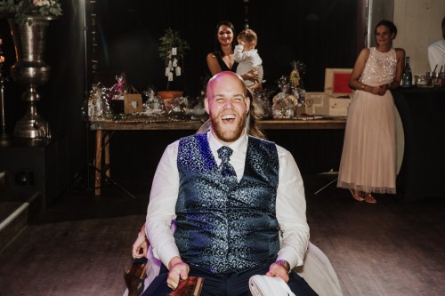 Ein Bräutigamsitzt auf einem Stuhl und lacht herzlich.