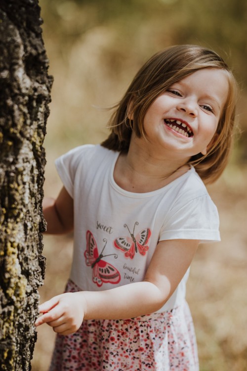 Ein kleines Mädchen steht hinter dem Baum.