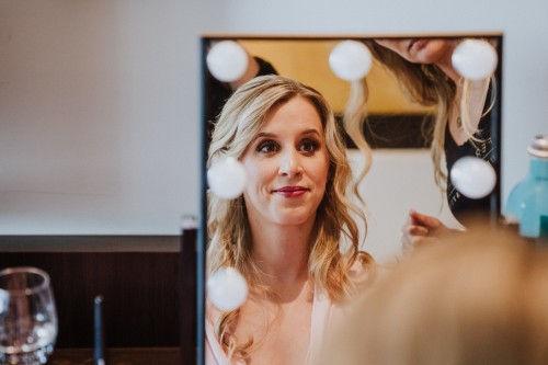 Eine Frau sitzt vor einem Spiegel und wird geschminkt.