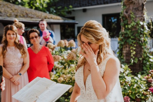 Eine Braut steht vor einer Gruppe von Menschen und wischt sich eine Träne im Gesicht ab.