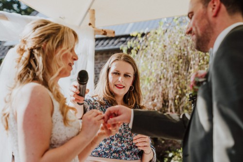 Ein Brautpaar steckt sich die Eheringe an und eine Frau hält das Mikro.