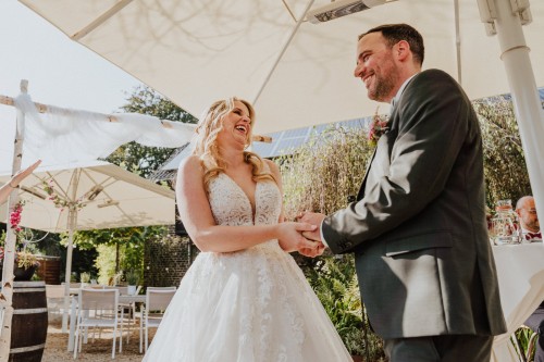 Ein Brautpaar steht unter einem Sonnenschirm und hält sich an den Händen.