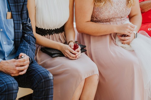 Hochzeitsgäste sitzen auf einer Bank und halten kleine Fläschchen in den Händen.