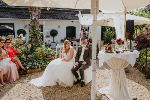 Ein Brautpaar und deren Gäste sitzen unter einem Sonnenschirm.