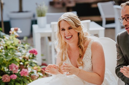 Eine Braut sitzt neben einen Bräutigam und lacht.