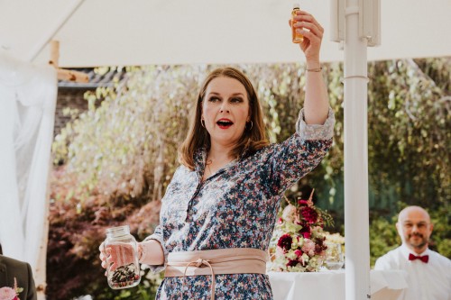 Eine Frau hält ein kleines Fläschchen in der Hand und bringt einen Toast aus.