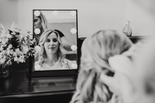 Ein schwarz-weißes Bild von einer Braut die vor einem Spiegel sitzt und gestyled wird.