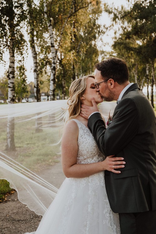 Ein Bräutigam küsst eine Braut in einer Birkenallee.