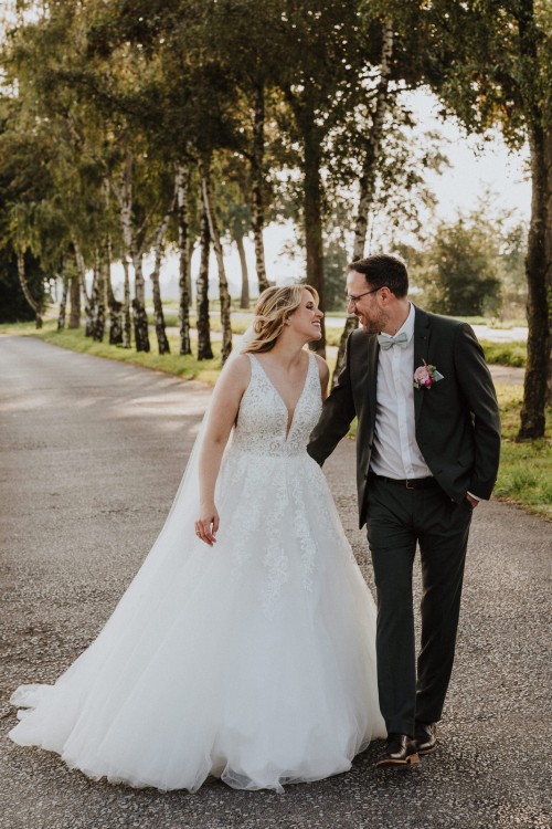 Ein Brautpaar spaziert durch eine Birkenallee.