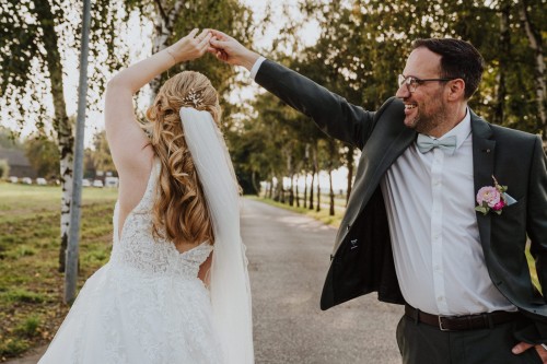 Ein Brautpaar tanzt in einer Allee.