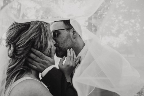 Ein schwarz-weißes Bild von einem küssenden Brautpaar unter einem Schleier.