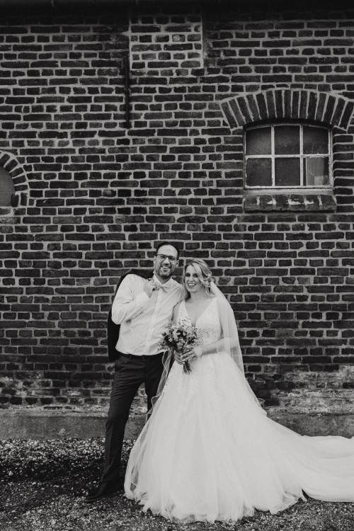 Ein schwarz-weißes Bild von einem Brautpaar vor einer Ziegelmauer.