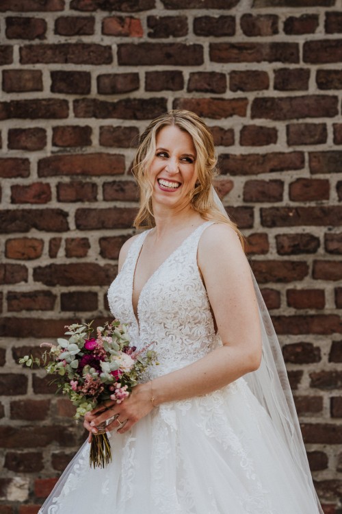 Ein Portrait von einer lächelnden Braut vor einer Ziegelmauer.