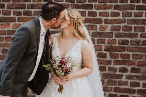Ein Brautpaar küsst sich vor einer Ziegelmauer.